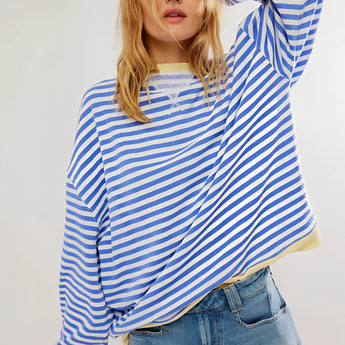 Red and white striped long sleeve crew neck blouse with button cuffs, worn by a person with shoulder-length hair, paired with shorts, showcasing a fashionable and casual look.