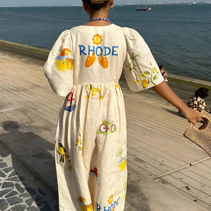 Woman wearing a RHODE dress, a women's cotton printed summer maxi with a fruit pattern, standing outdoors under a clear sky.