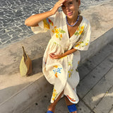 Woman wearing a RHODE dress, a women's cotton printed summer maxi with a fruit pattern, smiling and enjoying a sunny day with sunglasses, conveying a sense of happiness, leisure, and fun.