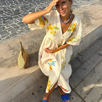 Woman wearing a RHODE dress, a women's cotton printed summer maxi with a fruit pattern, smiling and enjoying a sunny day with sunglasses, conveying a sense of happiness, leisure, and fun.