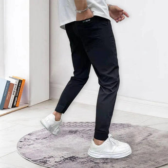 Men's black tapered track pants in a slim fit design displayed on a model. The pants feature a moisture-wicking fabric ideal for sportswear, with a focus on comfort and style. The image highlights the pants from waist to thigh, showcasing their sleek design and cool aesthetic suitable for athletic activities.