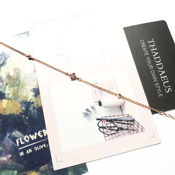 Rose gold bracelet with multicolor gemstones from Thaddaeus Jewelry displayed on a white paper background.
