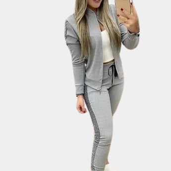
Women's luxury tracksuit in rose gold velvet with sequin details, shown in gray color, size XL. The outfit features long sleeves, a fitted waist, and a stylish collar, accessorized with sunglasses.