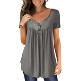 A woman standing and smiling, wearing a royal blue pleated scoop neck blouse with short sleeves.
