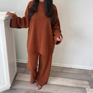 
A rust-colored wide-sleeve sweater and pants knit set, featuring a cozy loungewear design in dark brown, displayed in an XL size with a focus on the neck, sleeve, and waist areas. The background includes wooden flooring.