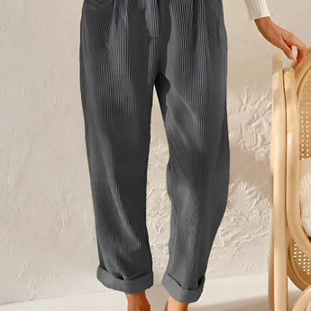 Gray high-waisted women's pleated pants in vintage style, made from corduroy fabric, worn by a person standing. The pants are designed with a focus on the waist and feature a relaxed fit around the thigh and knee areas.