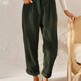 A woman standing and wearing green high-waisted pleated pants made from corduroy fabric, showcasing a vintage style.