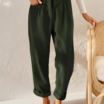 A woman standing and wearing green high-waisted pleated pants made from corduroy fabric, showcasing a vintage style.
