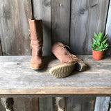 Rustic women's distressed brown leather zipper mid-calf boots placed on a wooden floor next to a potted houseplant.