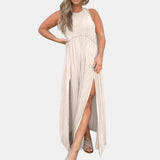 
A woman wearing a sage green sleeveless maxi dress that is styled as a casual beach sundress. The dress features a flowing design, perfect for a relaxed day out. She is smiling and standing in a relaxed pose, with attention to the dress's waistline and flowing length.