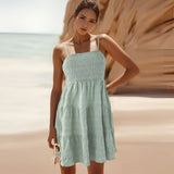 
A person wearing a sea green, knee-length tiered beach dress with spaghetti straps, showcasing a relaxed and summery look.