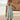 
A person wearing a sea green, knee-length tiered beach dress with spaghetti straps, showcasing a relaxed and summery look.