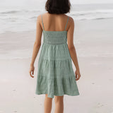 Sea green tiered beach dress with spaghetti straps, knee-length, worn by a woman standing by the water, showcasing the dress's flowing layers and a casual hairstyle.