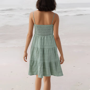 Sea green tiered beach dress with spaghetti straps, knee-length, worn by a woman standing by the water, showcasing the dress's flowing layers and a casual hairstyle.