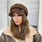 A woman wearing a brown sherpa baseball cap, styled as fashionable winter headgear, paired with a beige blazer.