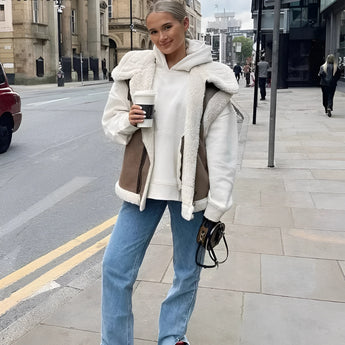 Sherpa fleece vest in camel color with buckle detailing, worn by a woman in XL size, styled as part of a chic streetwear ensemble. The vest features sleeveless design, showcasing a fashionable look, with the wearer standing in a confident pose.