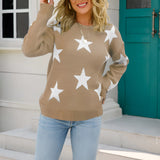 Blue and white star pattern crewneck sweater being worn by a person with a smiling expression; the sweater features long sleeves and is styled casually, seen in an indoor setting with a window in the background.
