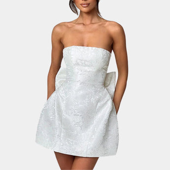 Strapless white satin cocktail dress with a lace overlay and large bow, worn by a person.