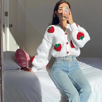 Women's trendy V-neck strawberry knit cardigan featuring long sleeves, paired with blue jeans, black hair, and eyewear.