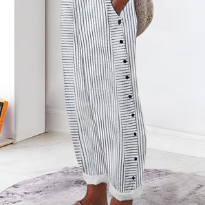 Striped button-up lounge pants in grey, styled for summer with lightweight fabric; shown on a model standing indoors on a wooden floor.