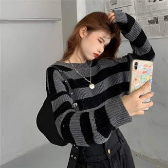 
A person wearing a trendy oversized black and white striped knit sweater, featuring long sleeves and a relaxed fit, perfect for autumn fashion.