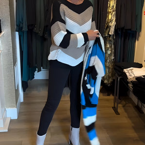 Woman wearing a chic autumn outfit featuring a striped sweater, black leggings, and white ankle boots, standing in a fashionable pose.
