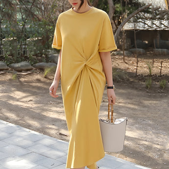 Stylish green tee featuring a knot detail and twisted design, showcasing short sleeves and a round neckline, modeled by a person standing outdoors among plants.