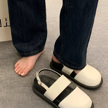 Stylish women's black platform orthopedic sandals with ankle strap being worn by a model dressed in denim trousers, standing on a grey floor.