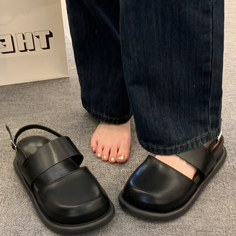 Stylish women's black platform orthopedic sandals with ankle strap, featuring a comfortable design. The image shows the sandals being worn with grey denim trousers, highlighting their fashionable appeal.