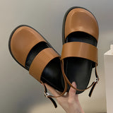 A pair of stylish women's black platform orthopedic sandals with ankle straps, designed for comfort, showcased on a model's feet while seated on a chair.