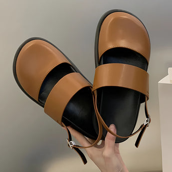 A pair of stylish women's black platform orthopedic sandals with ankle straps, designed for comfort, showcased on a model's feet while seated on a chair.