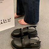 Stylish women's black platform orthopedic sandals with ankle strap, shown on a person wearing jeans, standing on a grey floor.