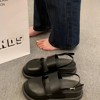 Stylish women's black platform orthopedic sandals with ankle strap, shown on a person wearing jeans, standing on a grey floor.