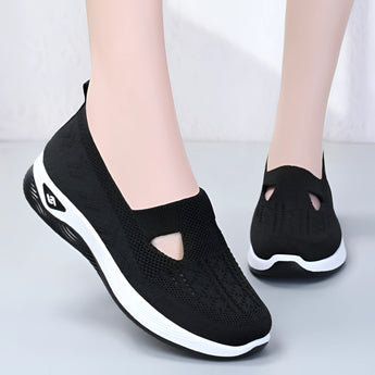 Stylish women's black slip-on sneakers, lightweight and breathable, showcasing a sleek design with flexible material for comfort, positioned on a human leg.