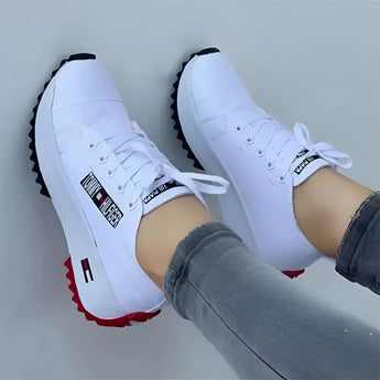 A pair of stylish women's white sneakers with a distinct red sole, being worn by a person dressed in casual urban fashion jeans, showcasing the trendy and sporty design.