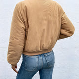 Tan corduroy bomber jacket for women, perfect for trendy fall outerwear, featuring a comfortable textile with a classic bomber style including full sleeves and a waist-length design, worn by a person standing, paired with jeans and a dress shirt.
