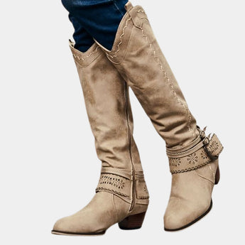 Taupe suede knee-high boots with a Western-inspired design, featuring a studded heel and a side zipper.