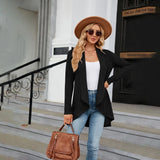 A person wearing a teal long sleeve knit cardigan, accessorized with a white fedora hat, sunglasses, and carrying a stylish bag.