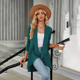 Teal long sleeve knit cardigan worn by a model, showcasing its fall fashion design with emphasis on shoulder, sleeve, and waist detailing. The cardigan appears to be part of a chic layered outfit suitable for cooler weather.