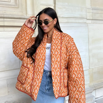 
A stylish textured bomber jacket in a monochrome design, shown in orange, size large. The jacket is worn by a person accessorized with sunglasses, highlighting a trendy winter street style. The focus is on the upper body, showcasing the outerwear's texture and fit around the shoulders and neck.