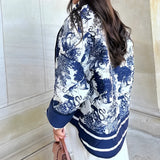 A blue textured bomber jacket in a monochrome winter street style worn by a person. The jacket features a stylish collar, long sleeves, and a comfortable fit, highlighting the waist and shoulders.