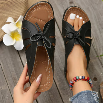 
A pair of trendy green women's flat sandals featuring a bow-tie design, worn by a model.