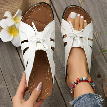 Trendy green women's flat bow-tie beachwear sandals in white, shown on a person's foot, highlighting the design and color against a bare skin backdrop.