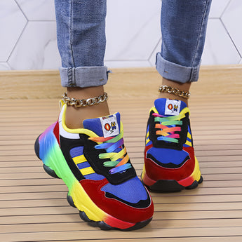 Multicolor sneakers with a rainbow sole, featuring vibrant colors like yellow, red, electric blue, and magenta, worn on a human leg. The main body of the shoe is white, highlighting the colorful sole design.