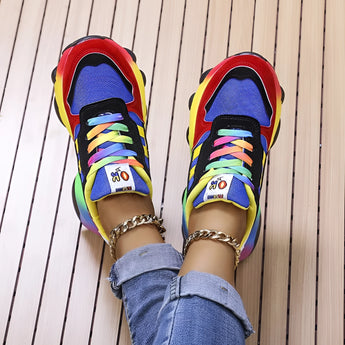 Trendy multicolor sneakers with a vibrant rainbow sole, worn by a person standing, showcasing the colorful plaid pattern on the sneakers.