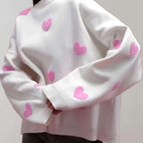 Cozy grey and pink heart pattern pullover for women, featuring long sleeves and a soft, comfortable fabric. This trendy pullover is designed with a stylish neck and collar, available in a size large, with a white and pink color scheme.