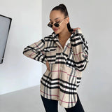 Oversized plaid jacket worn by a woman featuring a chic tartan pattern, with long sleeves, and styled as trendy autumn streetwear. The woman is wearing sunglasses and making a casual gesture, highlighting the jacket's relaxed fit around the shoulders and waist.