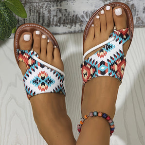 Boho chic summer sandals with a tribal pattern worn by a woman, showcasing the vibrant azure and intricate design. The image captures the sandals on a foot with a hand and part of the leg visible, set against a natural backdrop with plants, highlighting a fashionable and relaxed summer vibe.