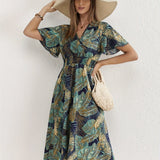 Tropical Leaf V-Neck Mini Dress in a bohemian style, featuring a lush green and white leaf pattern. The dress has short sleeves, a fitted waist, and a flared skirt, ideal for summer resort wear.