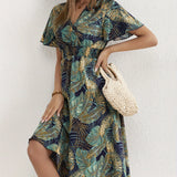Tropical Leaf V-Neck Mini Dress featuring a bohemian style, perfect for summer resort wear. The dress has a flattering fit with a v-neckline and short sleeves, showcasing a vibrant tropical leaf pattern. The model is posed with her hand on her hip, highlighting the one-piece garment's silhouette.